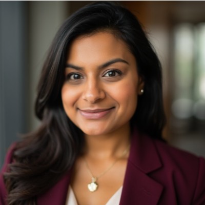 Sandia, a woman with dark hair wearing a burgundy blazer and a gold necklace, smiling warmly at the camera.